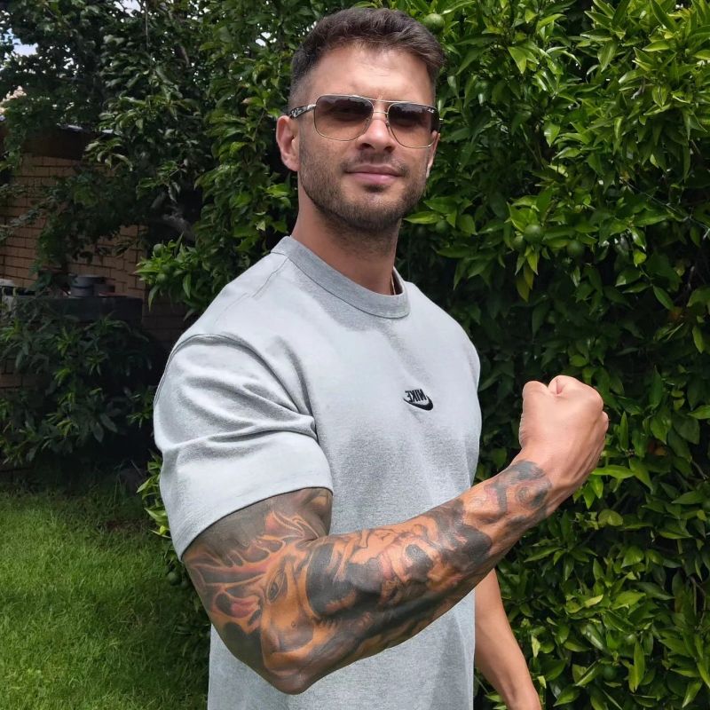 Man showing off a detailed sleeve tattoo while wearing sunglasses and a grey Nike shirt.