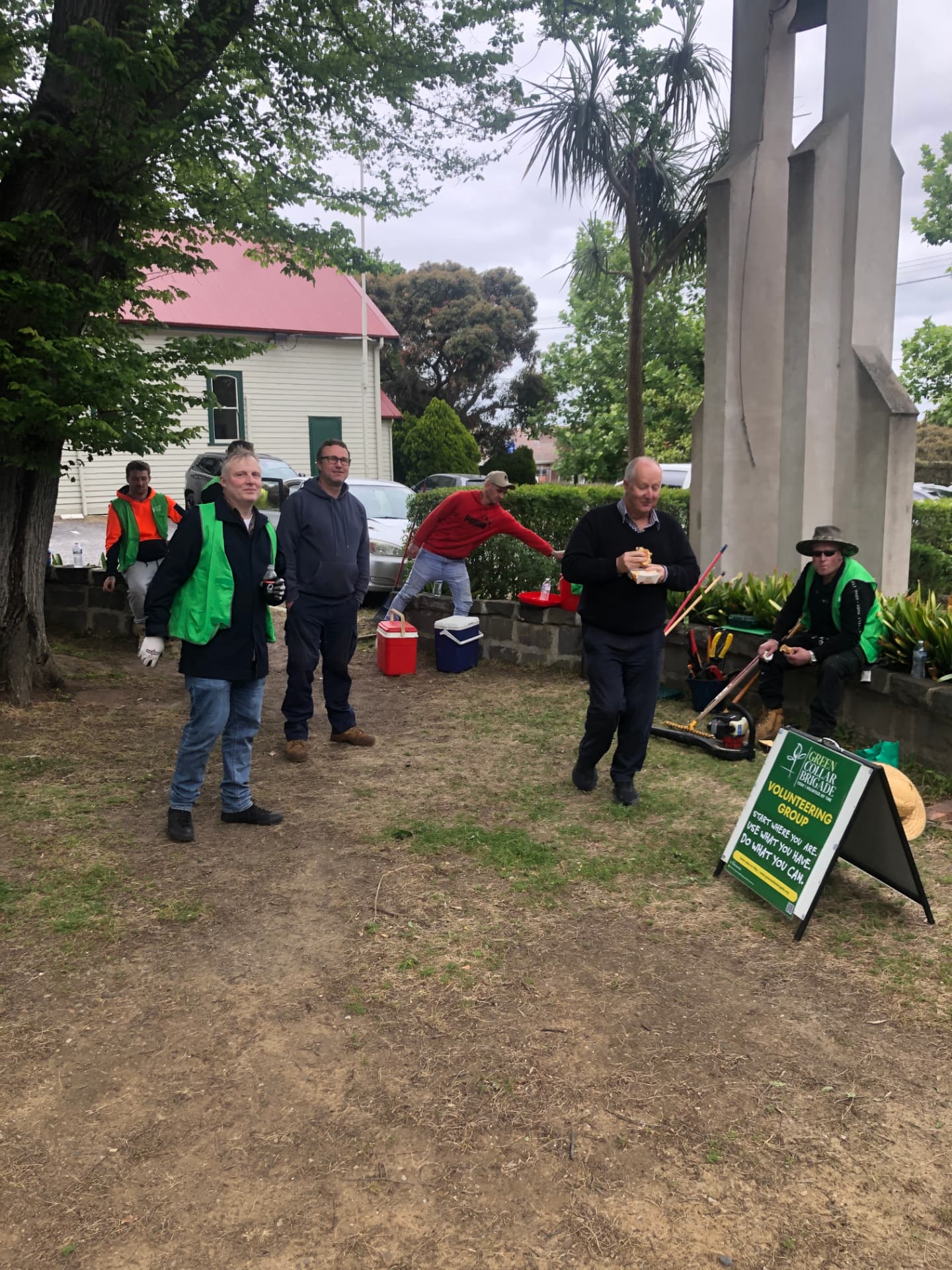 Brigade volunteers taking a lunch break beside the Volunteering Group sign and tools